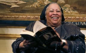 US author Toni Morrison (C) poses with her 1977 novel entitled "Song of Solomon" on September 21, 2012 during a reception sponsored by the US ambassador Charles H. Rivkin (R) at his residence in Paris, as part of the 10th America Festival.