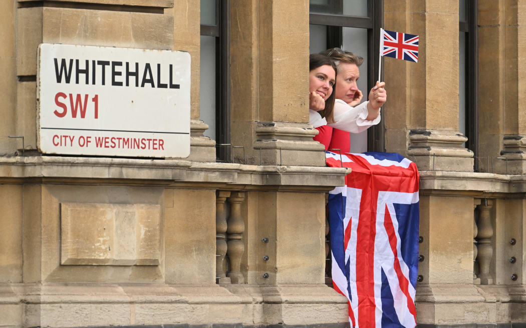 Onlookers view the proceedings from a window on Whitehall in central London on May 6, 2023, during the coronations of Britain's King Charles III and Britain's Camilla, Queen Consort. - The set-piece coronation is the first in Britain in 70 years, and only the second in history to be televised. Charles will be the 40th reigning monarch to be crowned at the central London church since King William I in 1066. Outside the UK, he is also king of 14 other Commonwealth countries, including Australia, Canada and New Zealand. Camilla, his second wife, will be crowned queen alongside him, and be known as Queen Camilla after the ceremony. (Photo by SEBASTIEN BOZON / POOL / AFP)