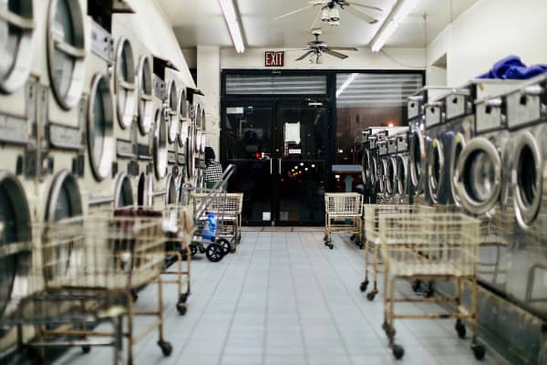 An image of an empty laundromat, with washing machines and empty laundry carts.