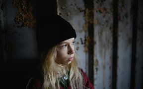A young blonde girl wearing a black beanie looks out a window.