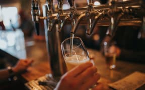 A person's hand can be seen holding a beer glass as the beer pours from a tap in a bar.