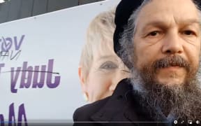 Whakatāne mayoral candidate Nándor Tánczos stands before a vandalised campaign sign.