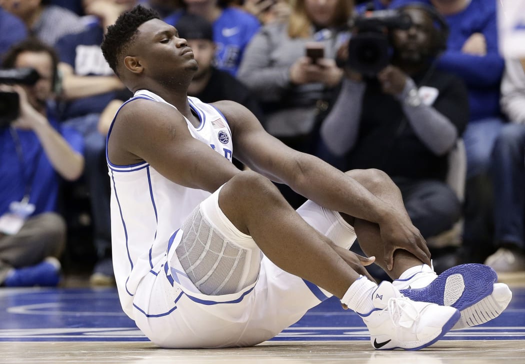 Duke's Zion Williamson sits on the floor following a injury during the first half of an NCAA college basketball game against North Carolina