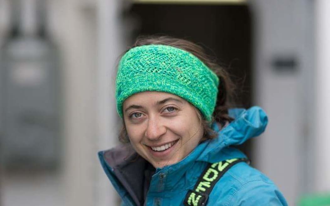 Sarah is pictured on the deck of a boat in a blue jacked with yellow overalls and a green headband.