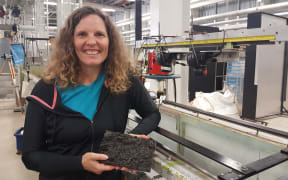 Engineer Heide Friedrich. She is holding a piece of moulded 'riverbed' covered in small pebbles. Water flowing above this rough riverbed is photographed and videoed using the cameras mounted above the flume.