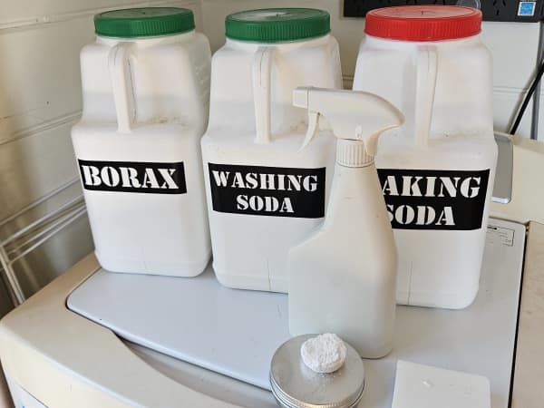 Three large white bottles labelled with Borax, Washing Soda and Baking Soda, plus a white spray bottle, sit on a washing machine.