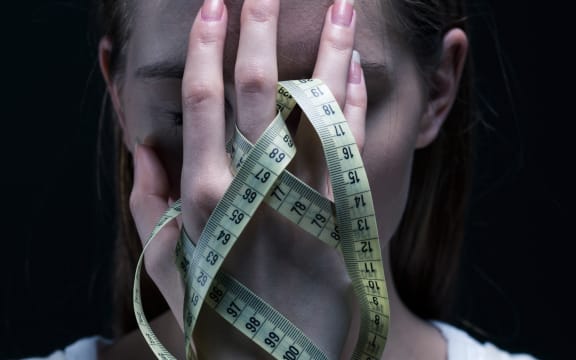 Anorexic girl covering her face with a centimeter