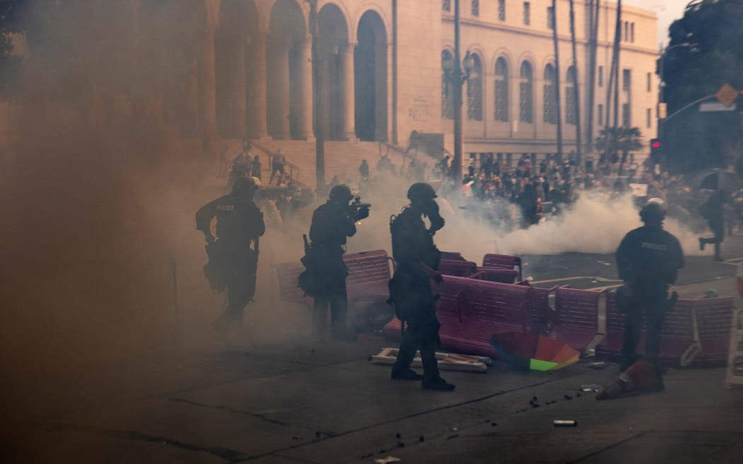 Los Angeles police officers advance on a makeshift barricade in a cloud of tear gas as clashes erupt with demonstrators next to City Hall during a protest following federal immigration operations, in Los Angeles, California on June 8, 2025. Demonstrators torched cars and scuffled with security forces in Los Angeles on June 8, as police kept protestors away from the National Guard troops President Donald Trump sent to the streets of the second biggest US city. (Photo by ETIENNE LAURENT / AFP)