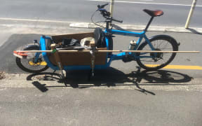 Marcus McShane has been using a broken broom mounted with some spare bamboo to sweep ahead of his wheels as he rides his cargo bike along the lane.