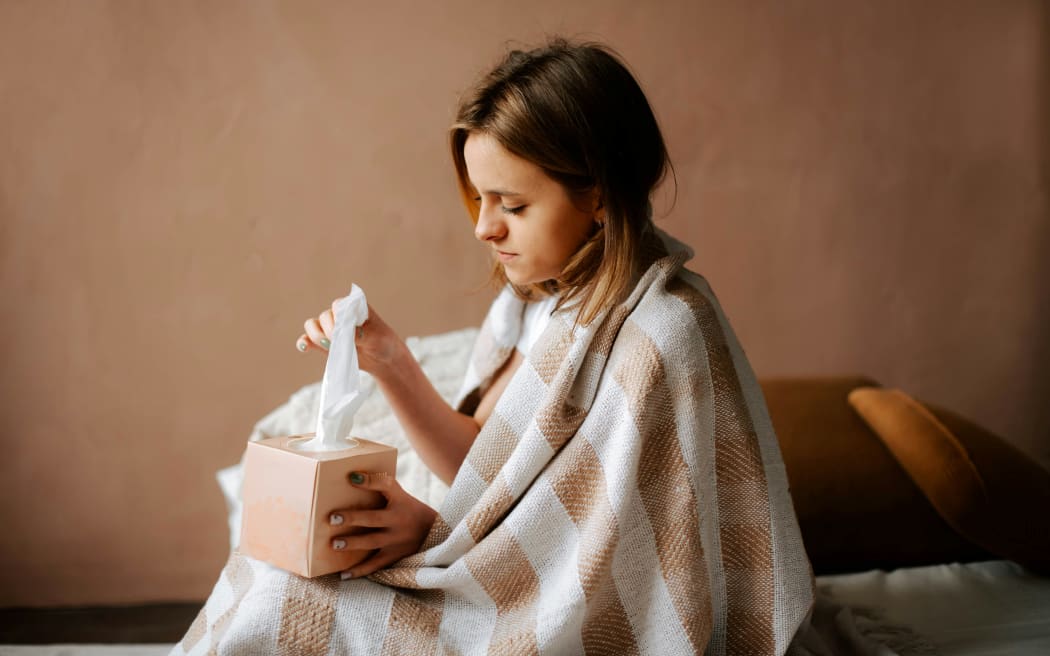 A sick person wrapped in a rug about to blow their nose