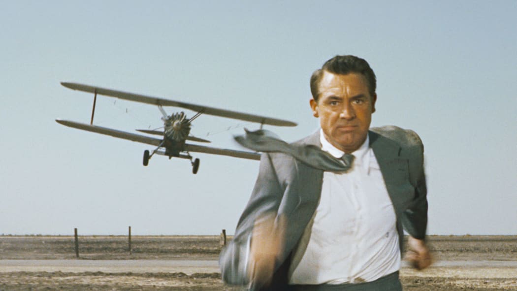 Movie still from Alfred Hitchcock's film North by Northwest featuring Cary grant being chased by a crop-dusting biplane.