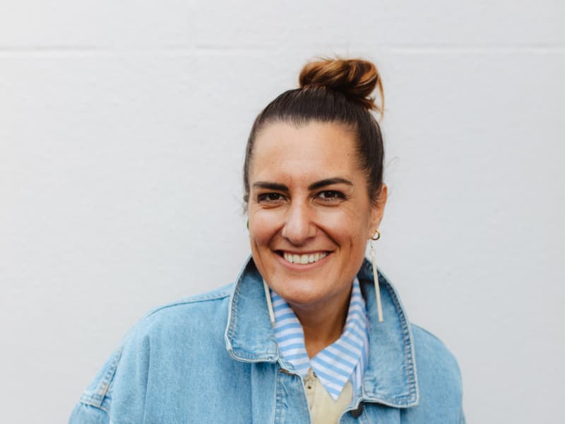 Qiane Matata-Sipu is a smiling woman with her hair pulled back, long white earrings and a pale denim jacket.