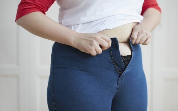 Woman trying to button jeans over tummy.