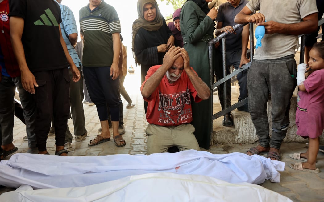 A Palestinian man mourns over the shrouded bodies of family members killed in an Israeli strike on a makeshift bakery housed in a tent on Al-Nassr Street in Gaza City on August 30, 2025, as they lie at Al-Shifa Hospital. The Israeli military declared Gaza City "a dangerous combat zone" on August 29 ahead of a looming offensive to conquer the Palestinian territory's largest city after almost two years of devastating war. (Photo by Omar AL-QATTAA / AFP)