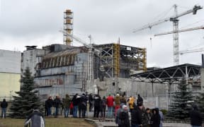 Visitors and journalists gather in front of a shelter and containment area built over the destroyed fourth block of Chernobyl's old nuclear power plant on December 14, 2015 in Chernobyl. -