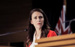 Jacinda Ardern stands at a press conference listening