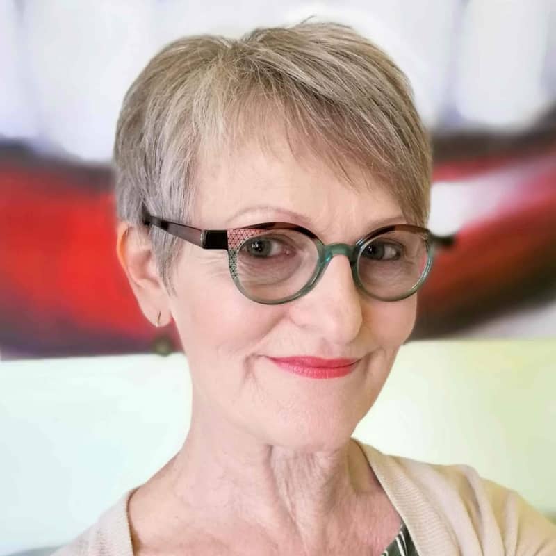 Fifi Colston is a slightly smiling woman with short grey hair and green-rimmed glasses.