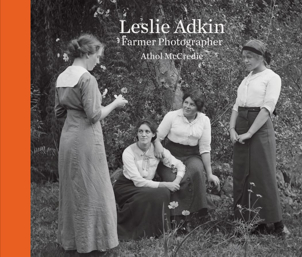 The front cover of a book of photography, called "LESLIE ADKIN - FARMER PHOTOGRAPHER", written by Athol McCreedie. A group of women talk in a circle outside in a garden.