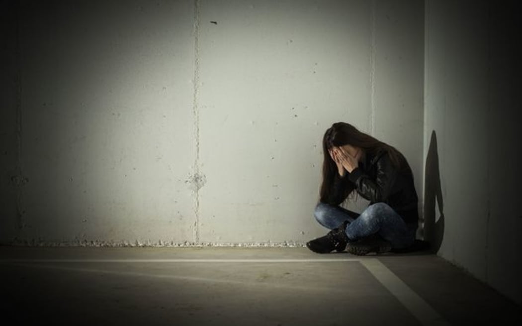 A photo of an upset teenager sitting slumped in a dark corner