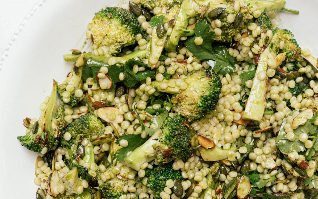 A close-up of a white plate. Packed into the centre is a bed of grains covered in greens.