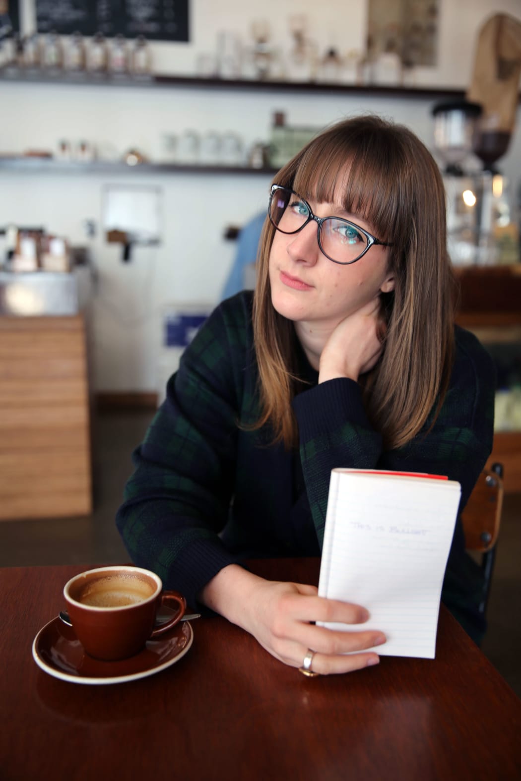 A picture of Louise Burston at a cafe holding a notebook