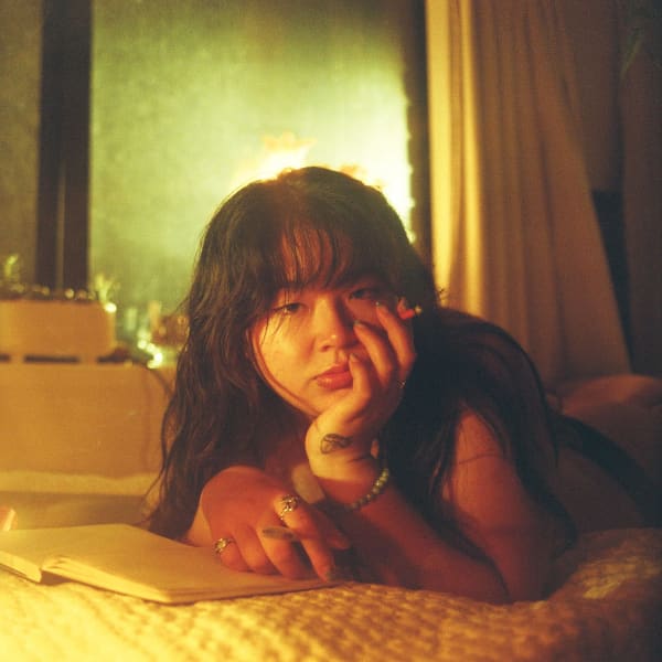 Crystal Chen - a young Asian woman with long hair lies on a bed facing the camera.