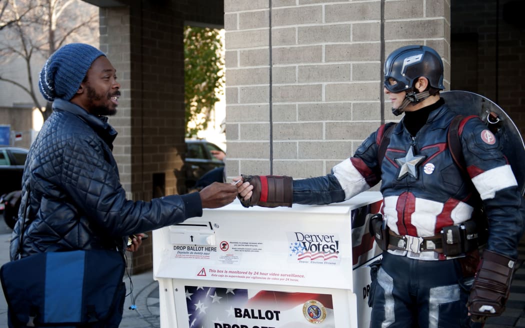 Matt Gnojek, aka Colorado Captain, hands out stickers to a voter in front of the Denver Elections Commission building .