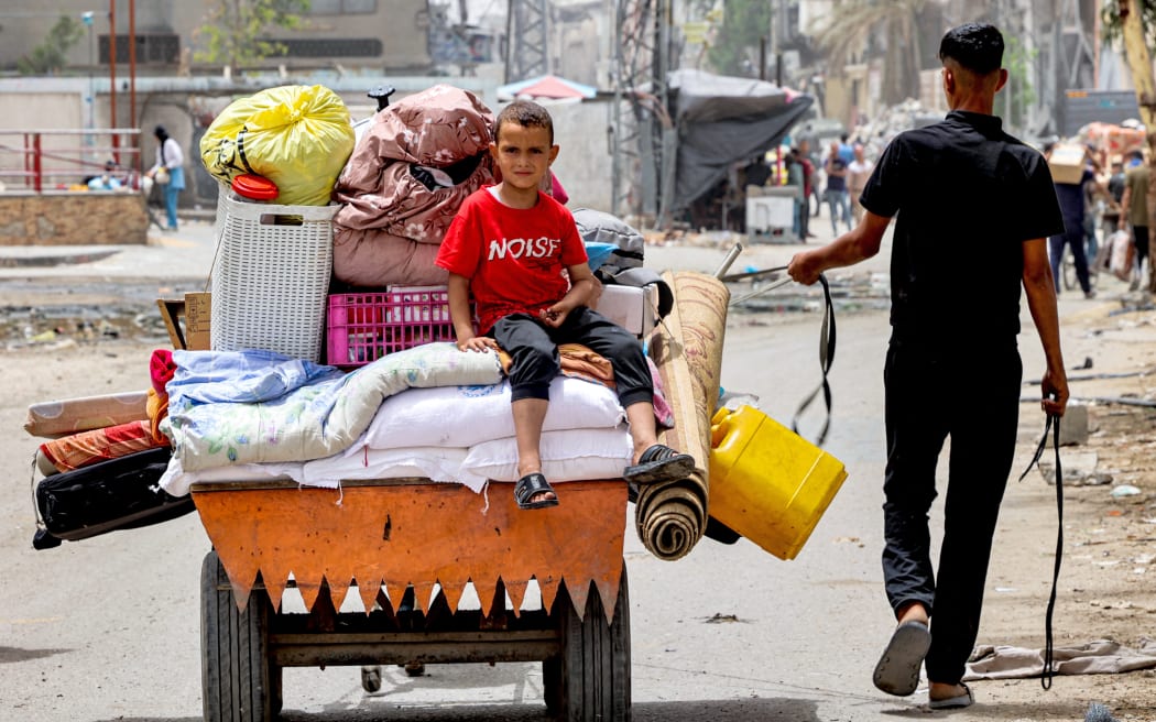 A boy sits atop cushions and mattresses loaded in the back of an animal-drawn cart led by a man as they evacuate from Sheikh Zayed in the northern Gaza Strip on 11 May, 2024 .