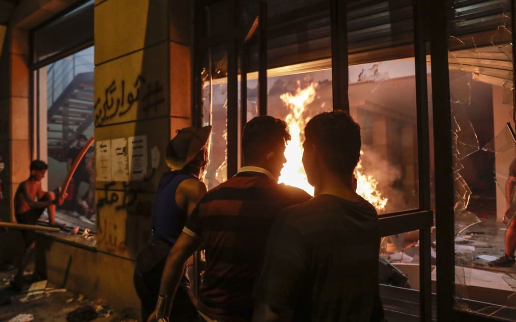 Lebanese protesters watch the flames inside the headquarters of the Lebanese association of banks in downtown Beirut on August 8, 2020,