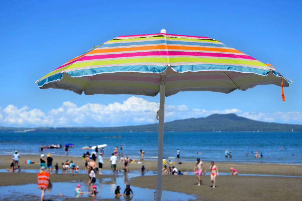 Colourful beach umbrella on a summer sunny day above unrecognizable people on a beach at the north shore of Auckland, New Zealand