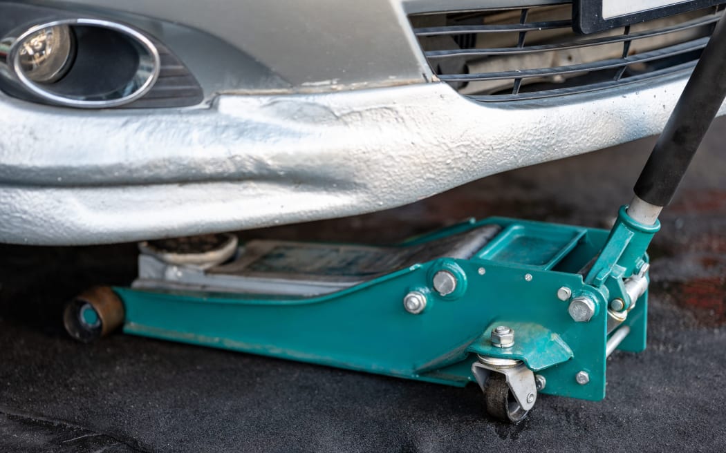 Green car jack or hydraulic floor jack, used for lifting vehicle.