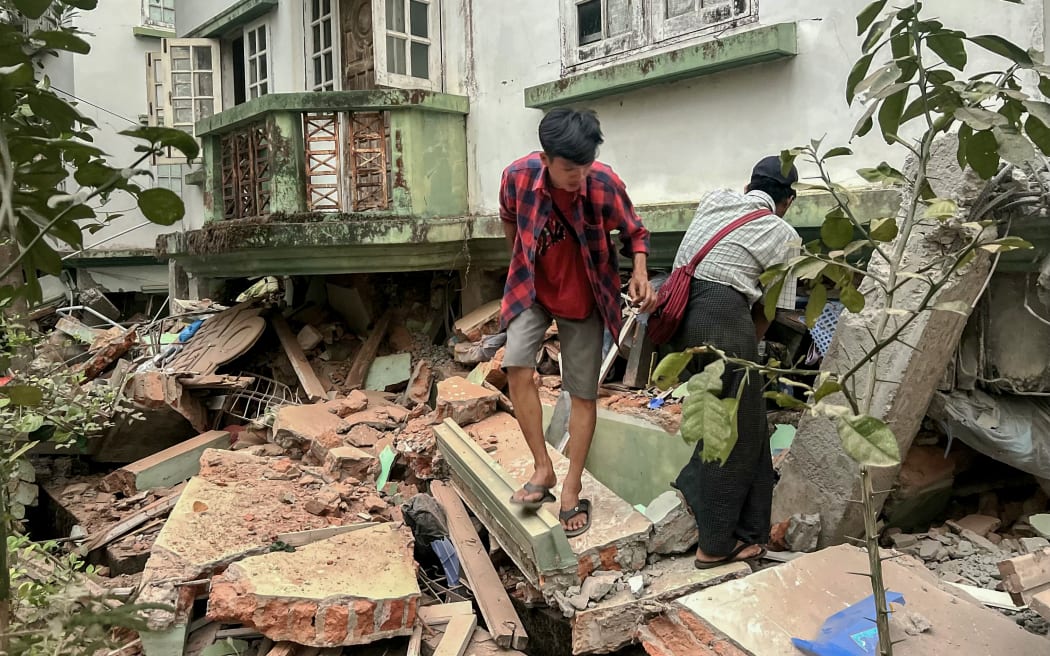Residents walk over debris next to a damaged building in Naypyidaw on March 28, 2025, after an earthquake in central Myanmar. A powerful earthquake rocked central Myanmar on March 28, buckling roads in capital Naypyidaw, damaging buildings and forcing people to flee into the streets in neighbouring Thailand. (Photo by Sai Aung MAIN / AFP)