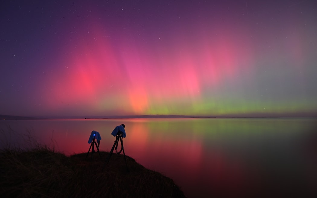 A photographer's camera setup is seen as the Aurora Australis, also known as the Southern Lights, glow on the horizon over waters of Lake Ellesmere on the outskirts of Christchurch on May 11, 2024. The most powerful solar storm in more than two decades struck Earth, triggering spectacular celestial light shows from Tasmania to Britain -- and threatening possible disruptions to satellites and power grids as it persists into the weekend.