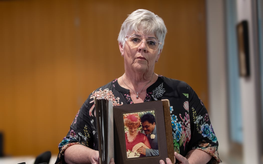 Image of a woman (Suzanne Young) holding a framed photograph of herself and her husband Darcy Te Hira.