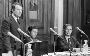 Prime Minister Bill Rowling delivers an outline of the Labour government’s economic policy in 1975 with ministers Colin Moyle (centre) and Michael Connelly (right) seated beside him. Rowling rejected retrenchment and defended heavy overseas borrowing as necessary to protect New Zealanders’ jobs.