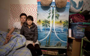Zhuang Qiuli and her boyfriend Feng Tao sit on the bed in their basement apartment in Beijing.