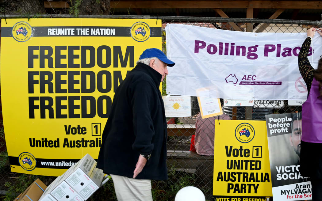 An election official (R) erects a sign as people prepare to cast their votes in Melbourne on May 21, 2022 as polling centres open in Australia's federal election. - Polls opened in Australia's federal election May 21, 2022 , with Prime Minister Scott Morrison fighting for another three-year term that would extend a decade of conservative rule. (Photo by William WEST / AFP)