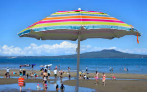 Colourful beach umbrella on a summer sunny day above unrecognizable people on a beach at the north shore of Auckland, New Zealand