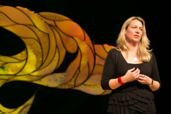 Woman stands on stage with a microphone.