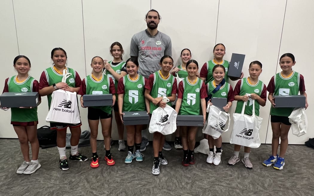 Steve Adams  behind presents the Rotorua U12 girls' basketball team with the new shoes they've just been given.