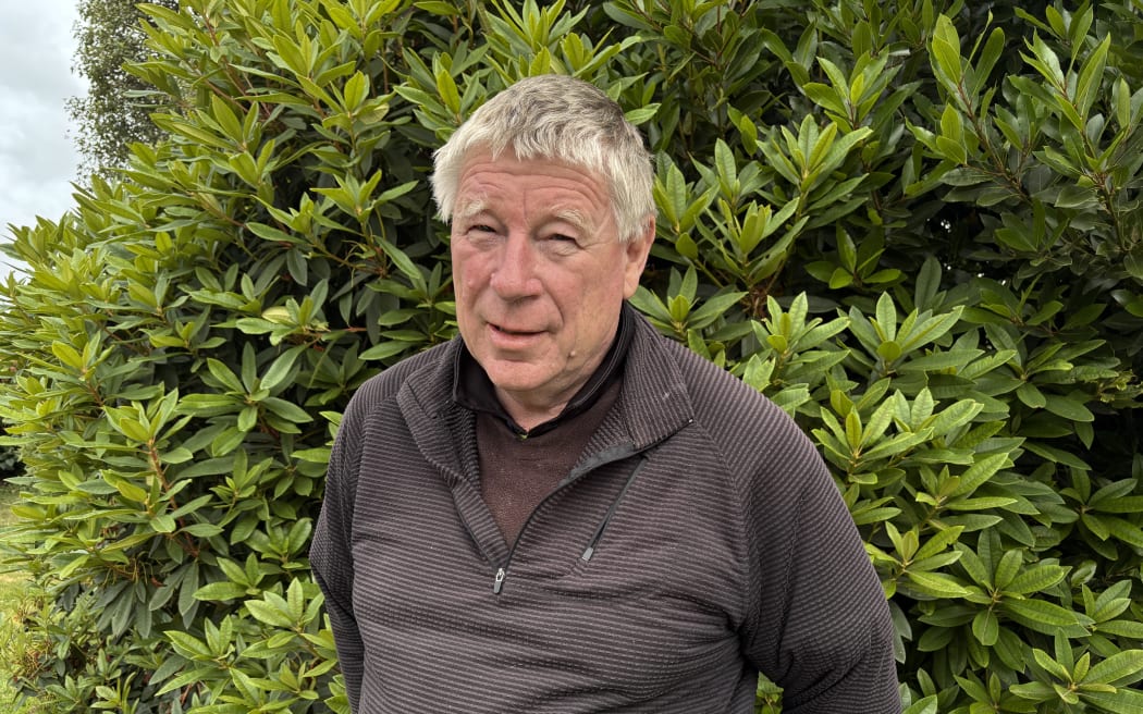A man looks at the camera standing in his garden.
