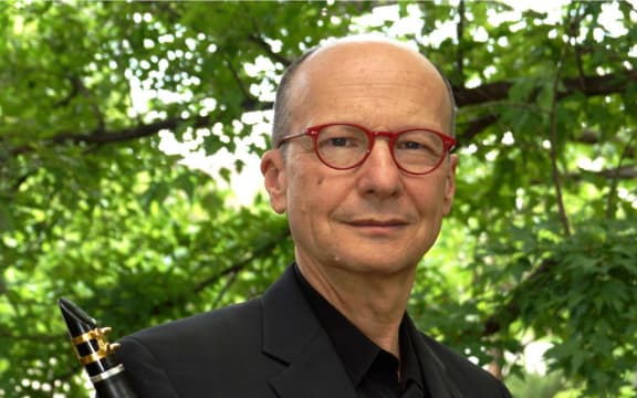 Clarinettist James Campbell with his clarinet in front of green tree foliage