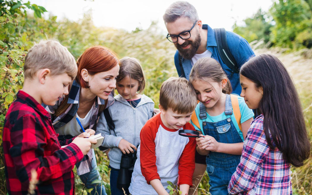 A group of small school children with teacher on field trip in nature, learning science.