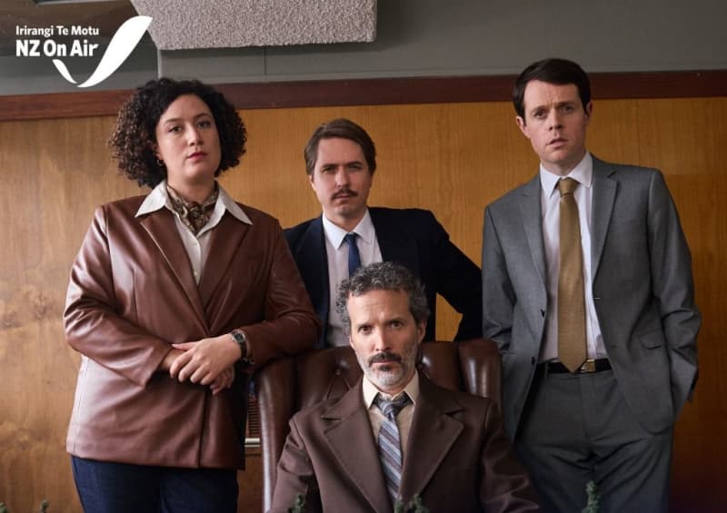 A group of four people in unattractive office clothing give tough looks to the camera. Text reads 'New Zealand Spy, brand new in 2026'