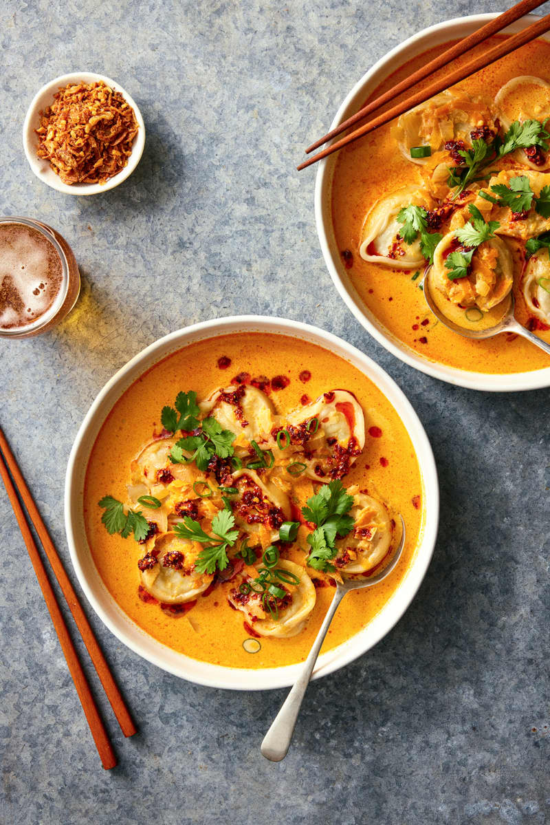 A bowl of red curry soup and dumplings.