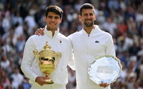 Spain's Carlos Alcaraz holding the winner's trophy (L) and second-placed Serbia's Novak Djokovic pose for pictures during the price ceremony at the end of their men's singles final tennis match on the fourteenth day of the 2024 Wimbledon Championships at The All England Lawn Tennis and Croquet Club in Wimbledon, southwest London, on July 14, 2024. Defending champion Alcaraz beat seven-time winner Novak Djokovic in a blockbuster final, with Alcaraz winning 6-2, 6-2, 7-6. (Photo by ANDREJ ISAKOVIC / AFP) / RESTRICTED TO EDITORIAL USE