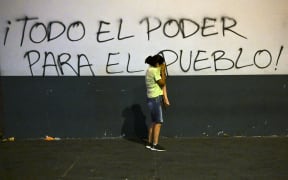 A demonstrator protects herself from tear gas next to a wall reading "All the power to the people!" during a protest against the government of President Dina Boluarte, in Lima on January 20, 2023. - Thousands of protesters began marching through Peru's capital on the eve to demand the president's resignation and fresh elections, following weeks of violent unrest that have left 44 people dead. The explosion of unrest began high up in the Andes and spread to Lima as indigenous people vented their fury over racism, polarization and growing poverty. (Photo by ERNESTO BENAVIDES / AFP)
