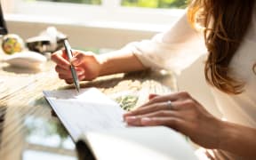 Businesswoman's Hand Signing Cheque On Wooden Desk