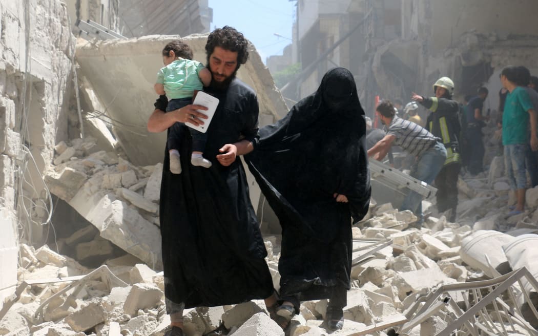 A family walks amid the rubble of destroyed buildings following a reported air strike on the rebel-held neighbourhood of al-Kalasa in the northern Syrian city of Aleppo, on April 28, 2016.