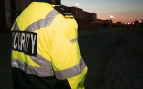 A person stands with their back to the camera in a high vis jacket which reads 'security'.